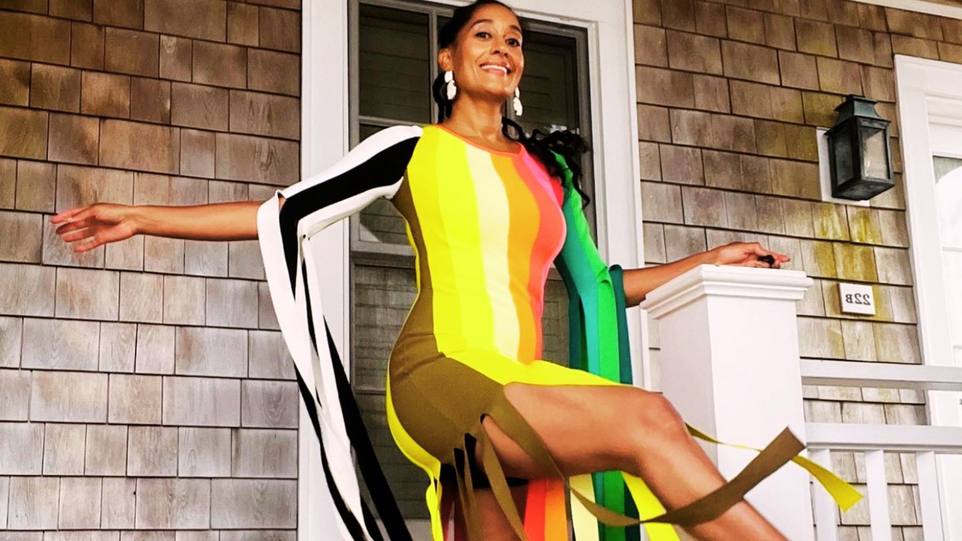 A woman in a vibrant dress poses confidently on a porch, showcasing her style and elegance.