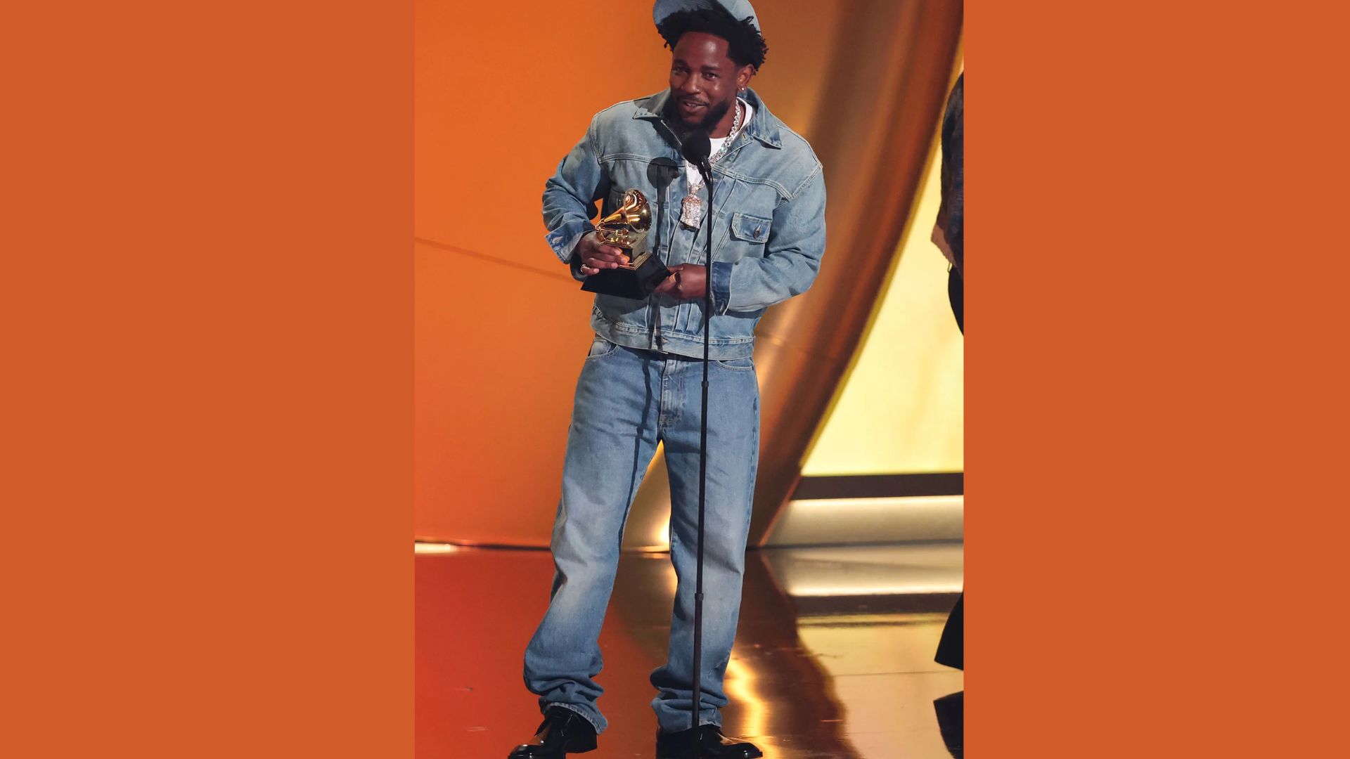 Kendrick Lamar in a blue jacket and jeans proudly holds an award, showcasing his style in the context of Kendrick Lamar's best looks.