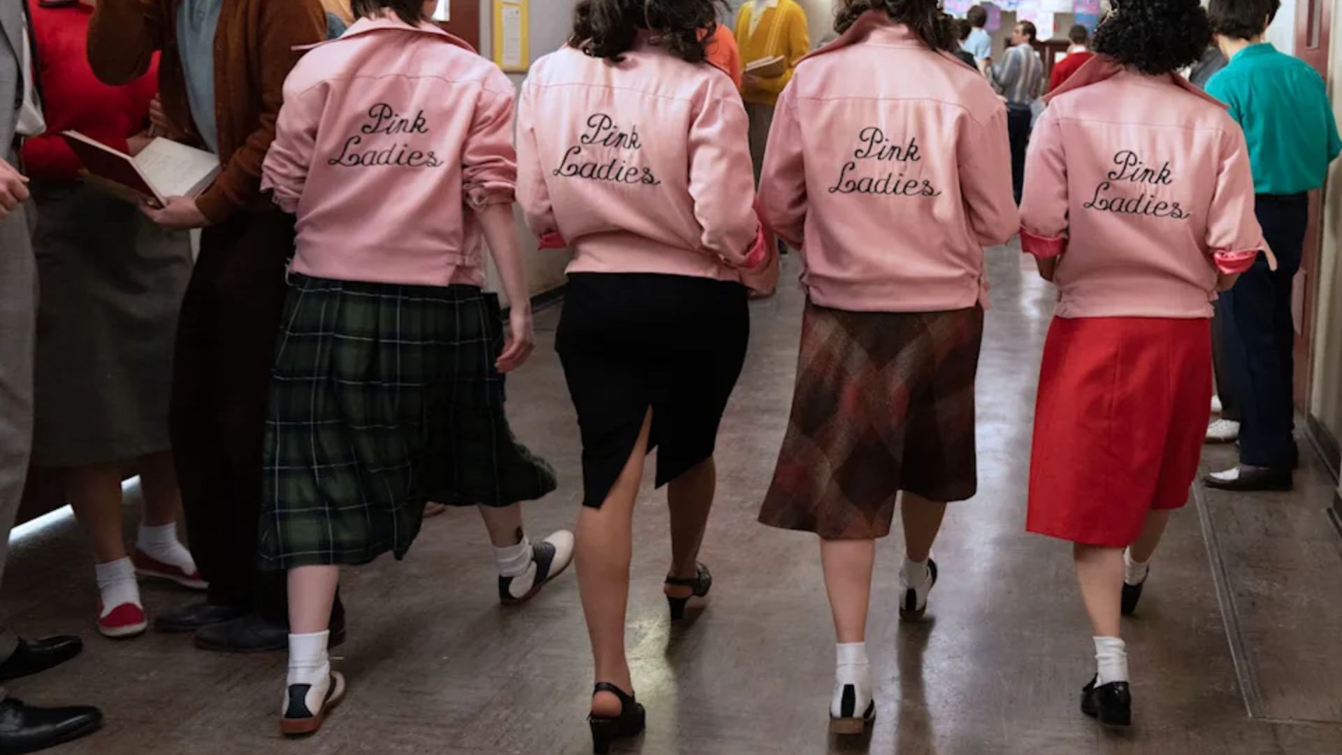 A group of women in pink jackets walking down a hallway, showcasing 50s fashion from the movie Grease.