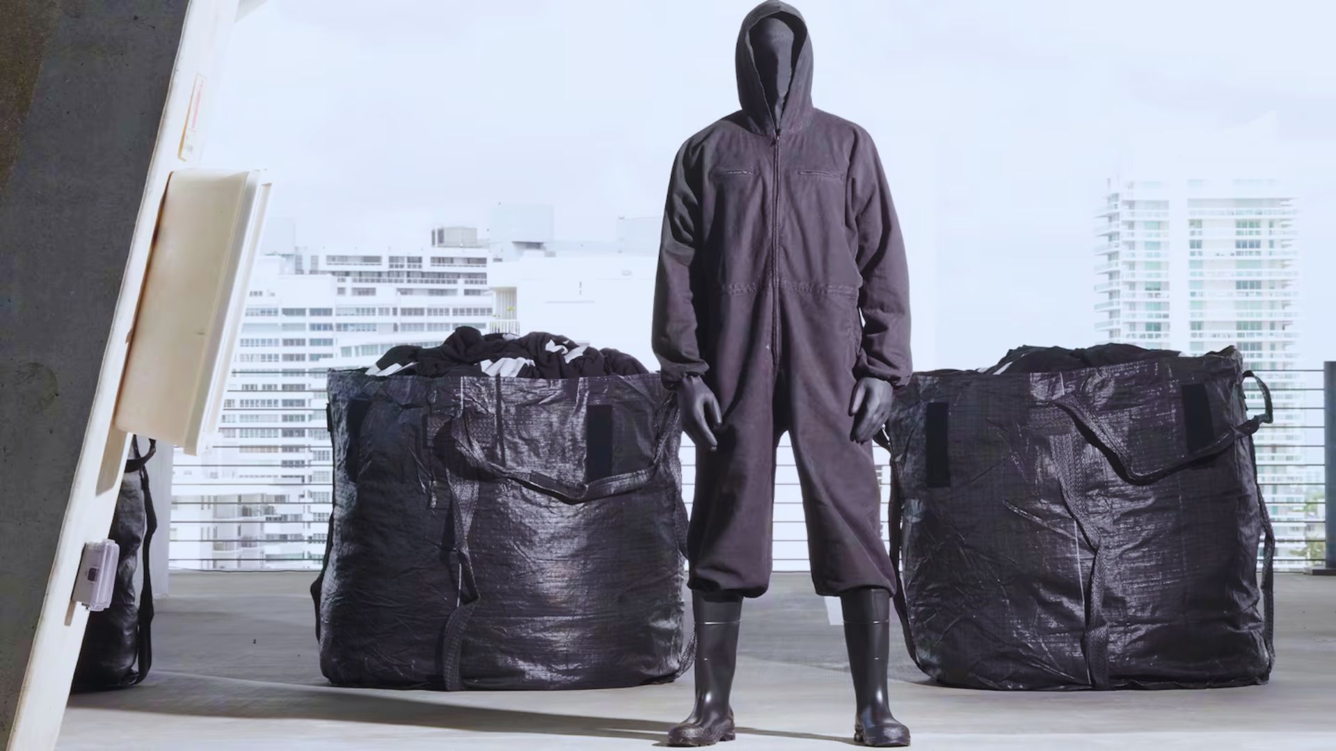 A man dressed in a black suit stands next to a collection of bags, exuding a professional demeanor.