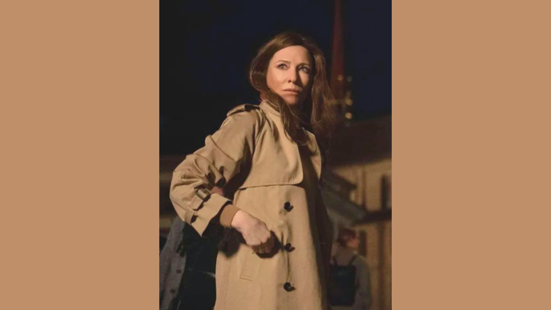 A woman in a trench coat stands confidently in front of a modern building, showcasing her stylish attire.