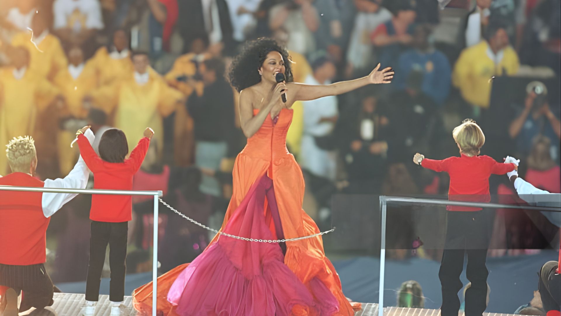 2. On stage, a woman wearing an orange dress performs a song, engaging the audience with her vibrant presence.