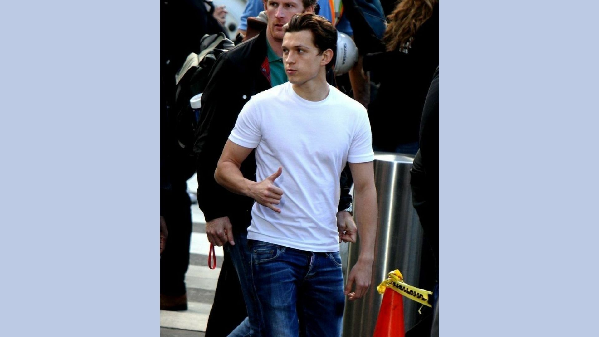 A man wearing a white t-shirt and jeans stands casually, showcasing a relaxed style.