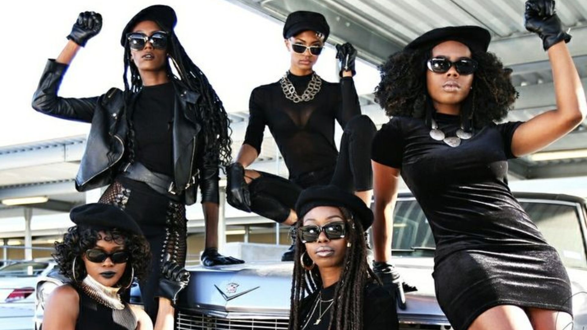 A group of women poses together, showcasing Black Panther Party-influenced outfits and styles for a photo.