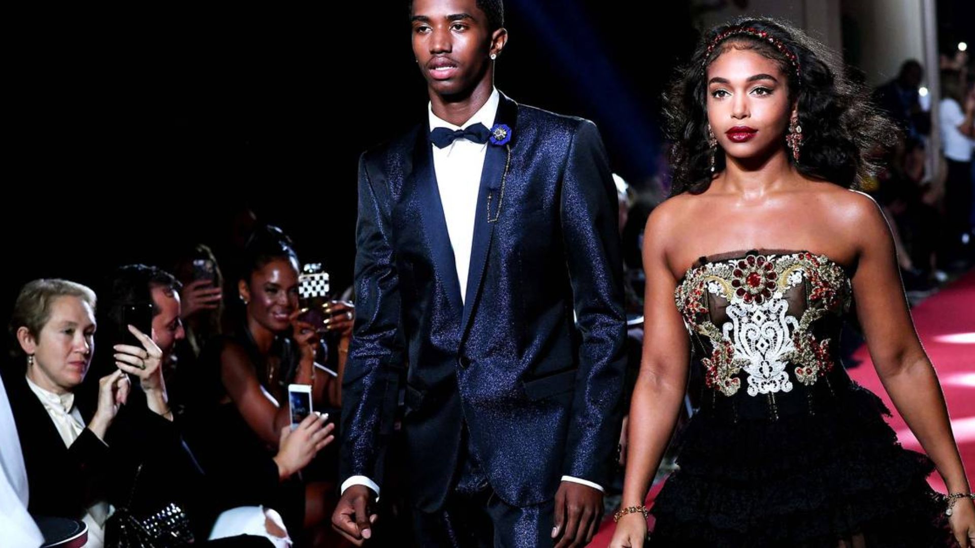 A man and woman elegantly walking together on a vibrant red carpet at a formal event.