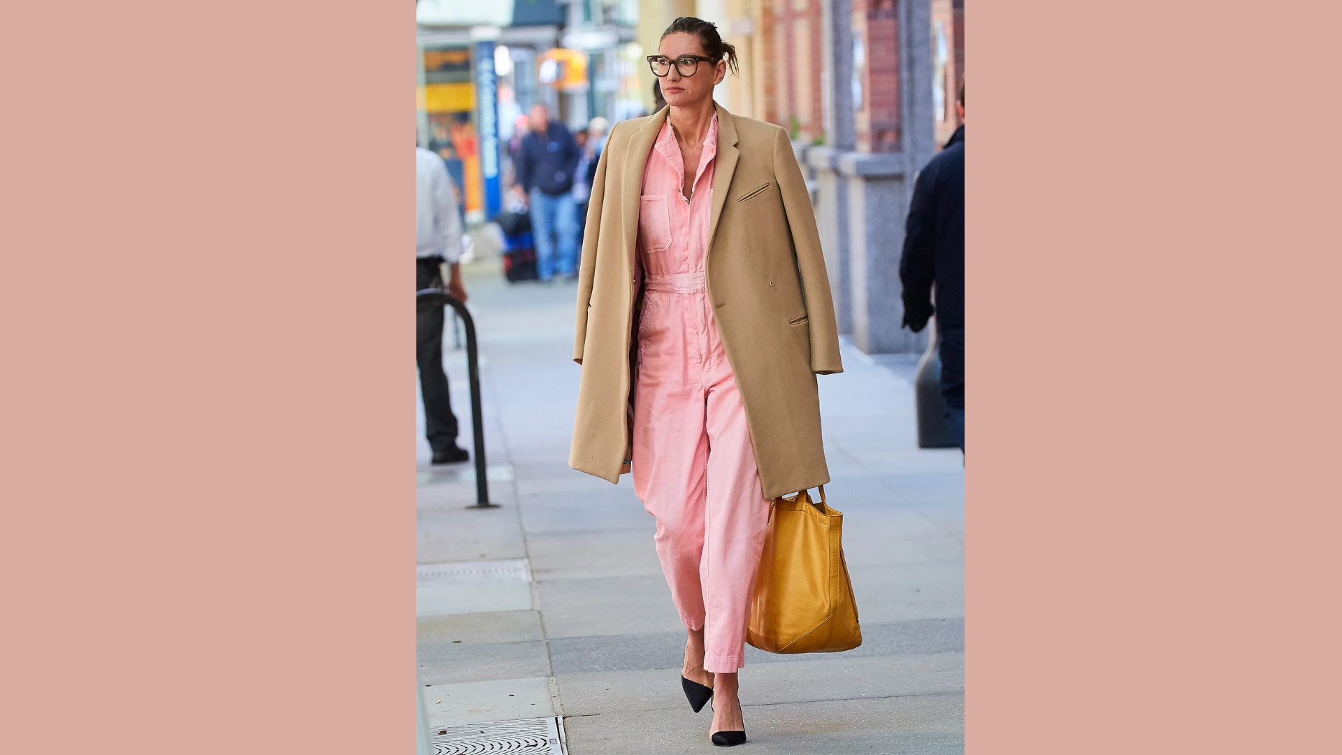 A woman dressed in pink pants and a coat walks leisurely down a city street.