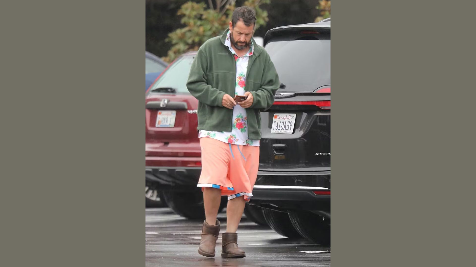 A man in a green jacket and pink shorts is walking along a path.