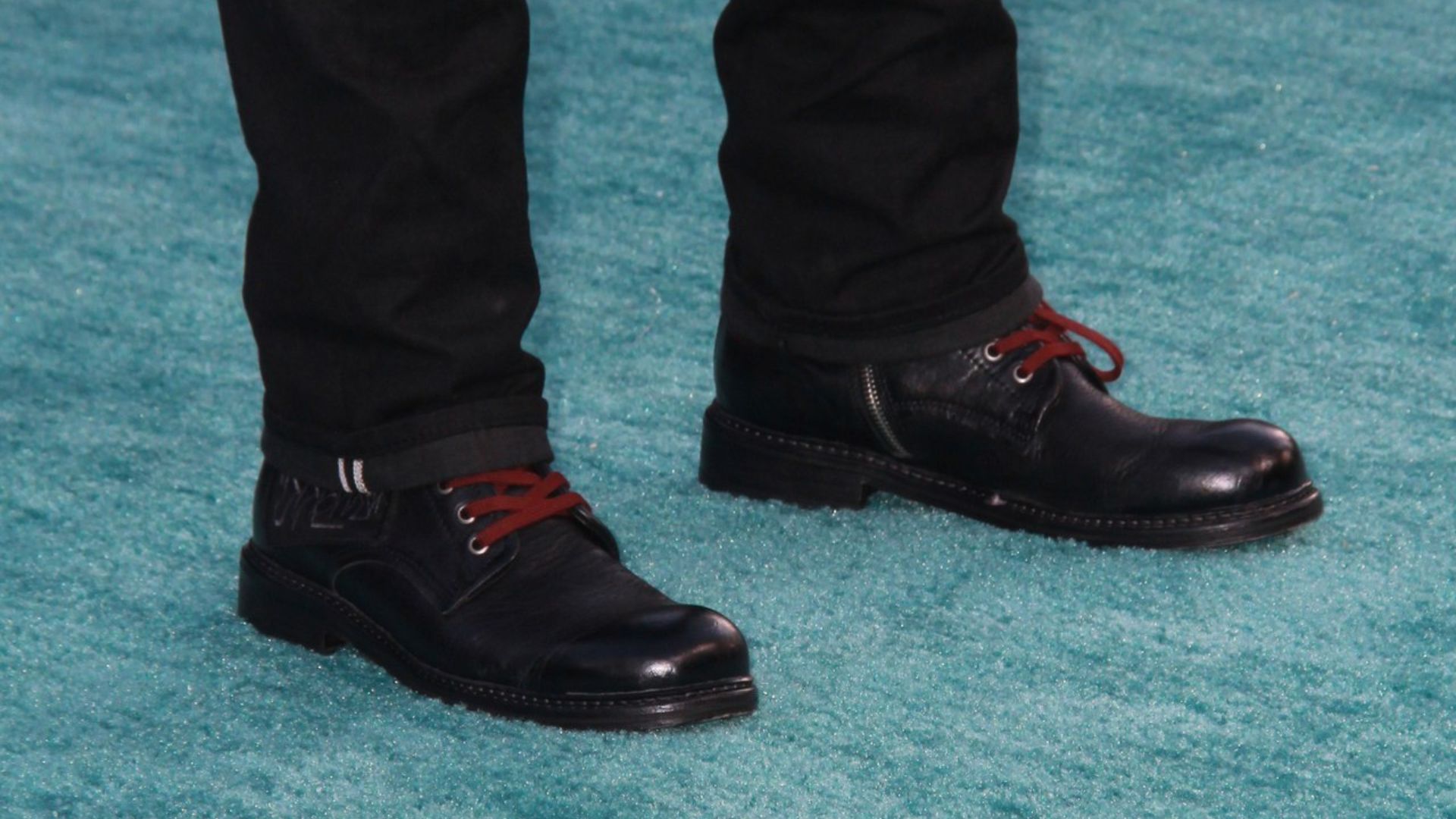 A person in black boots stands on a vibrant blue carpet, showcasing a stylish footwear choice against a colorful background.