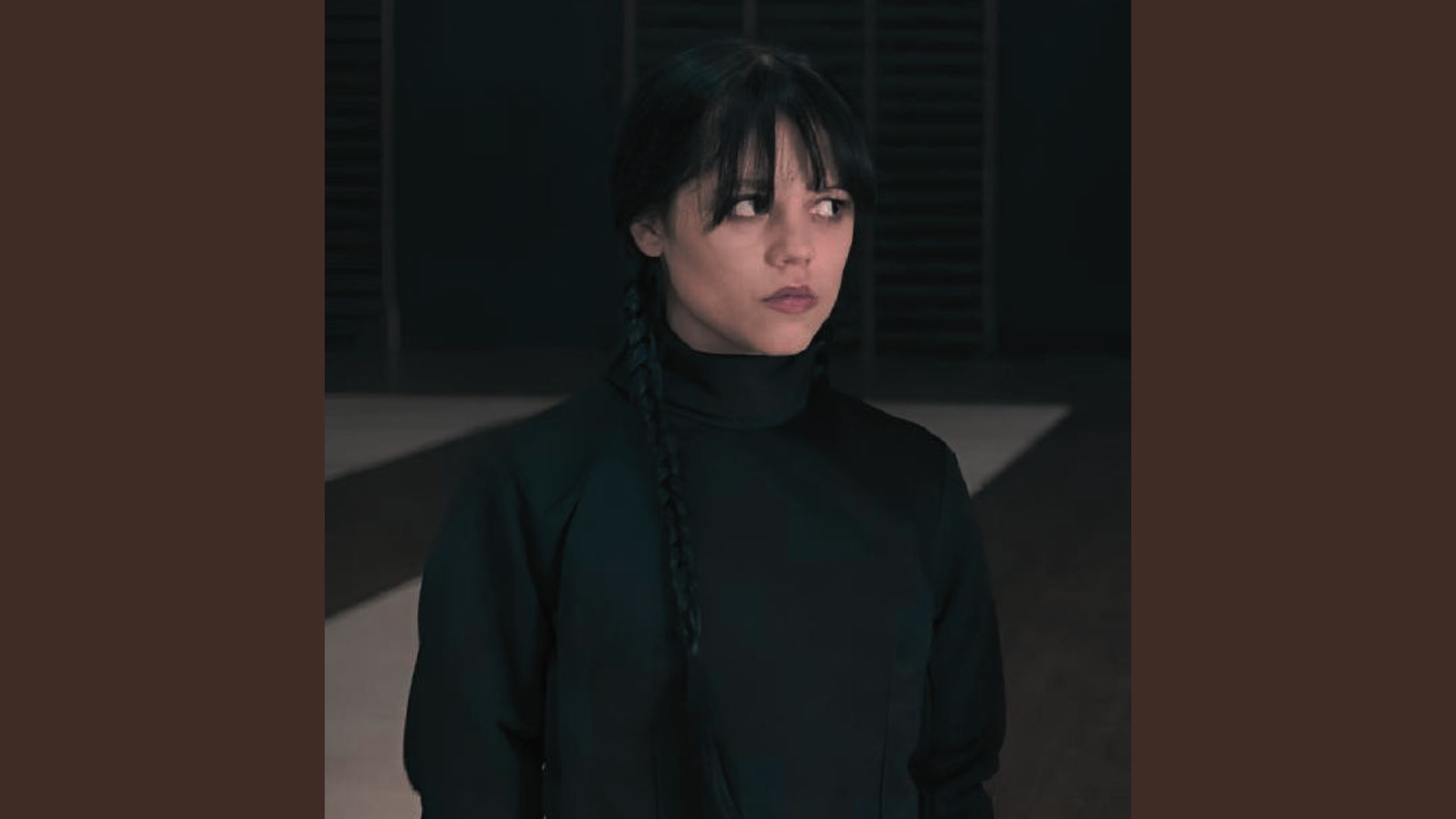 A woman in black turtleneck clothing stands in a stylishly decorated room, showcasing a layered fashion look.