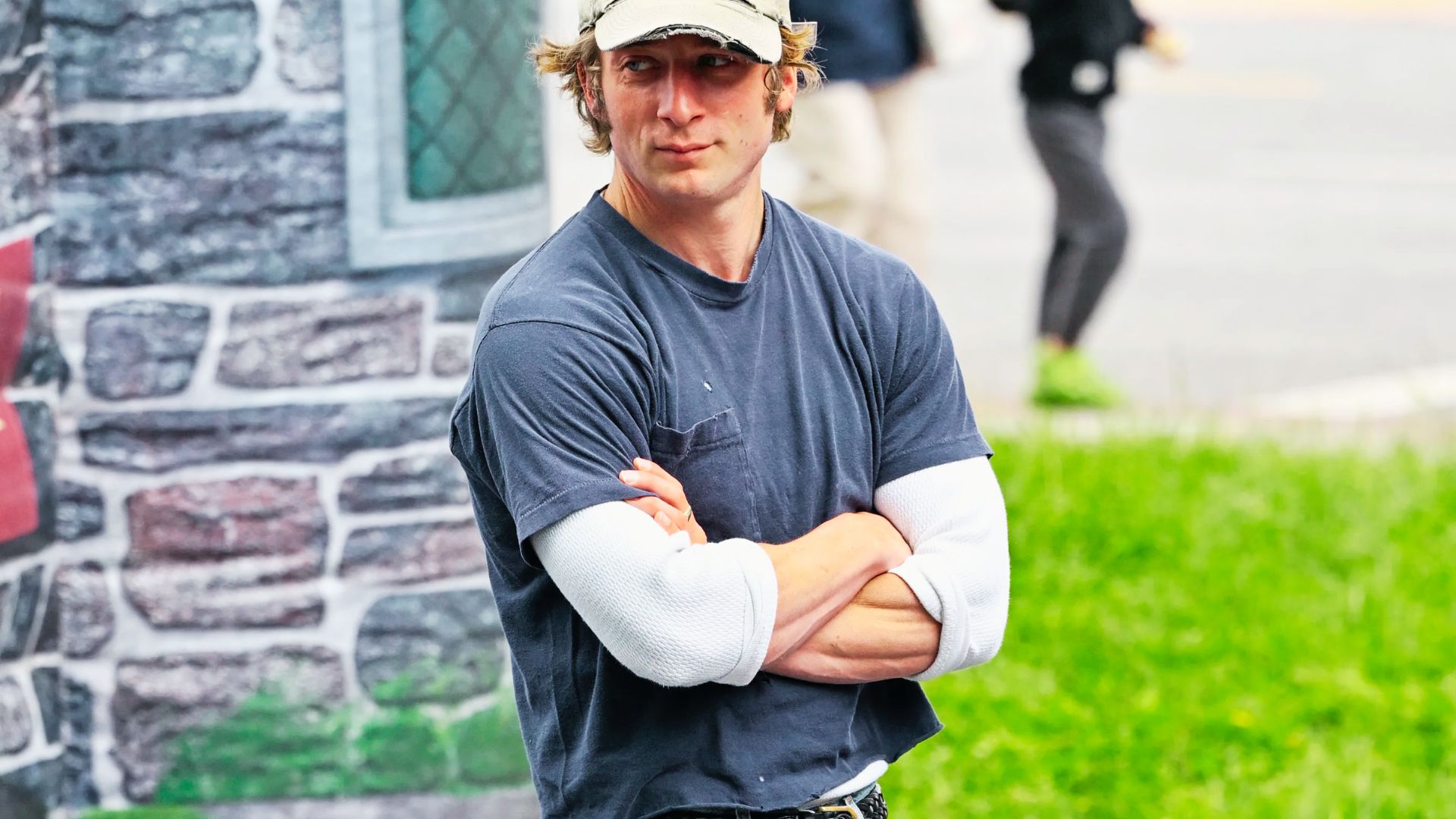 A man in a baseball cap stands in front of a building, showcasing elements of Jeremy Allen White's style.