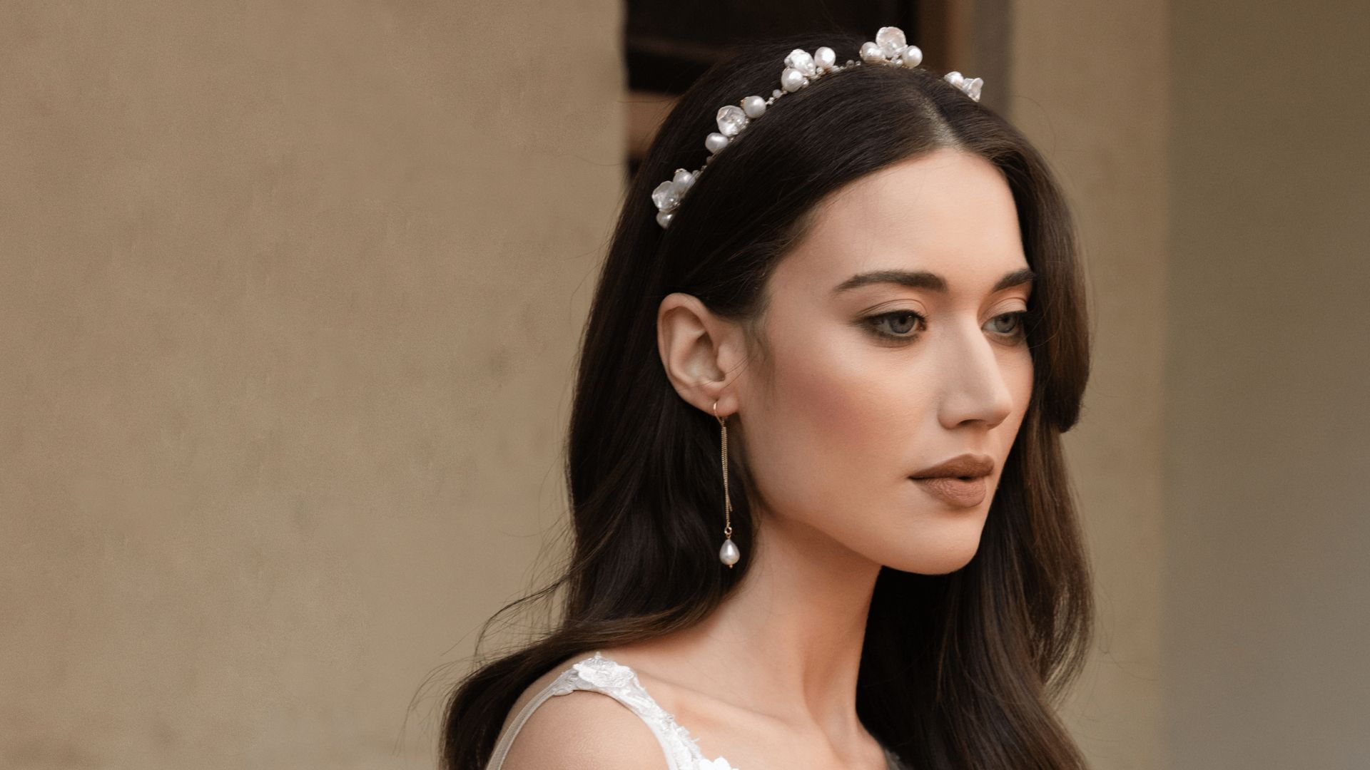 A woman in a white wedding dress and tiara, smiling gracefully, stands in a softly lit setting.