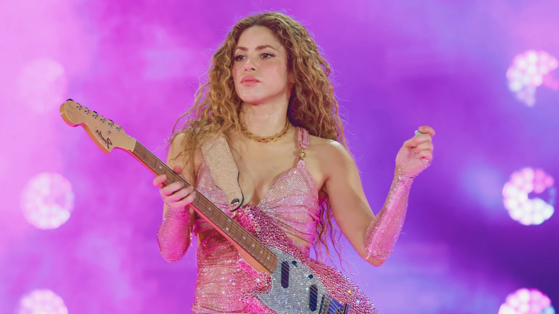 A woman in a pink dress performing with an electric guitar, showcasing her musical talent.