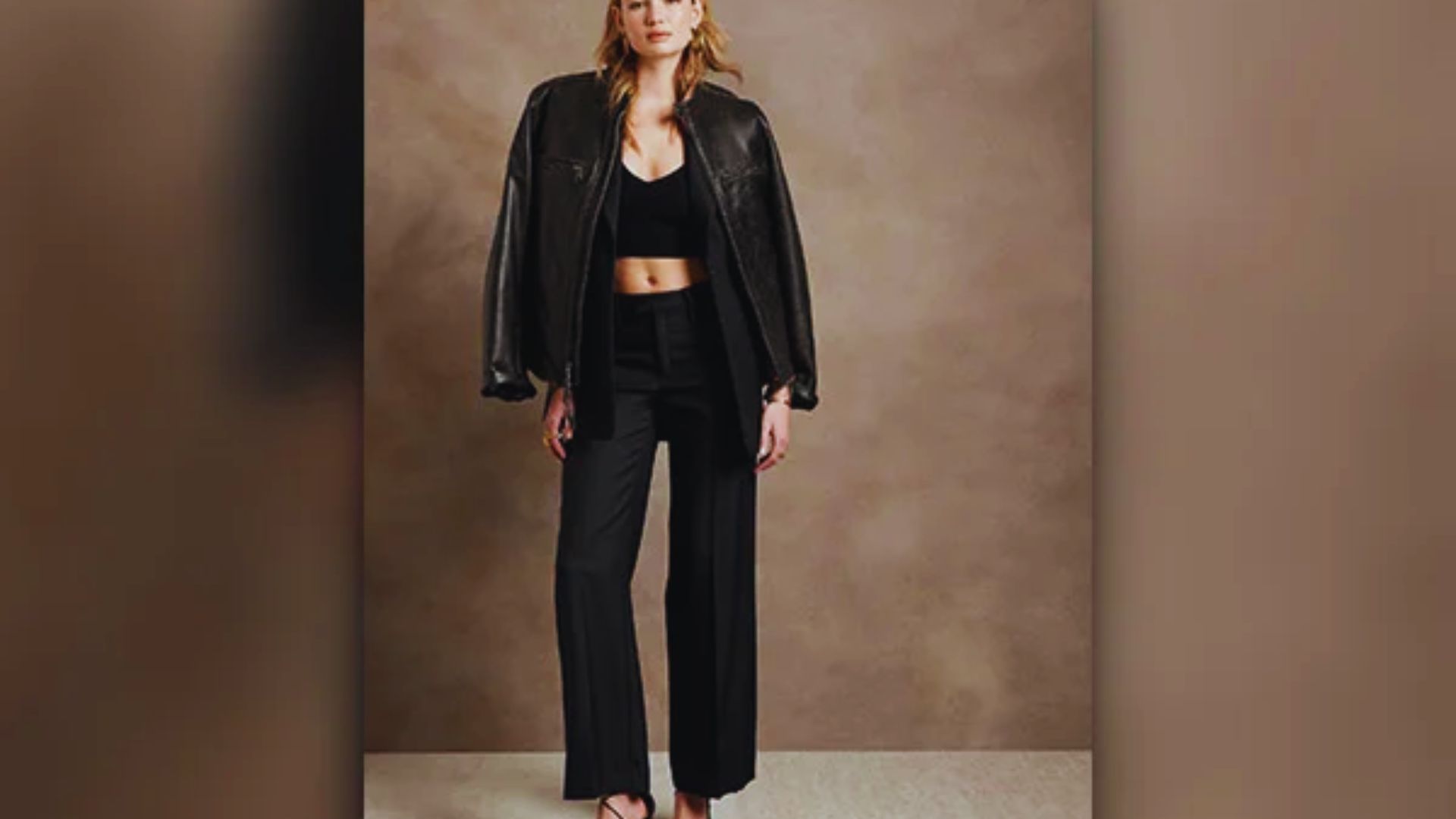 A model poses in stylish black pants paired with a trendy cropped top, showcasing a modern fashion look.