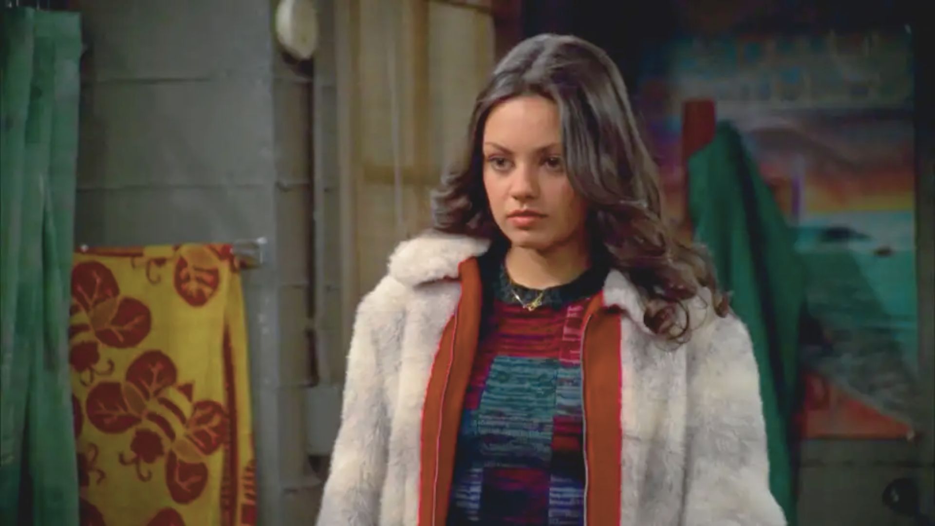 A woman wearing a fur coat and sweater stands in a well-decorated room, exuding elegance and warmth.