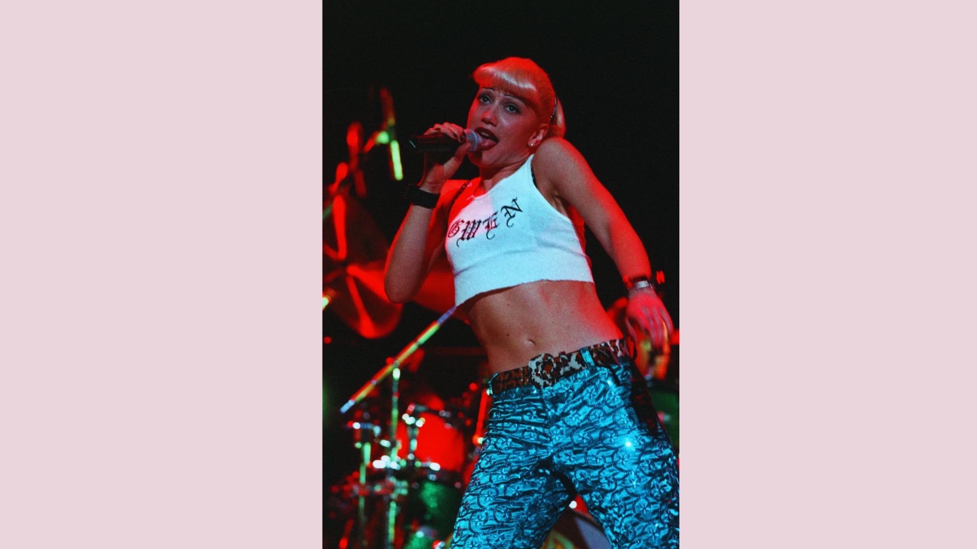 A woman wearing a white top and jeans stands confidently on stage, engaging with the audience.