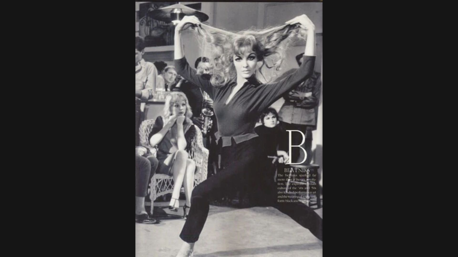 A woman dances joyfully in front of a colorful poster, showcasing her expressive movements and vibrant energy.