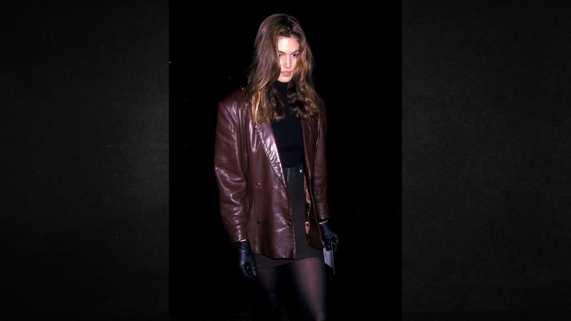 A woman wearing a leather jacket and black tights stands confidently, showcasing a stylish and edgy outfit.