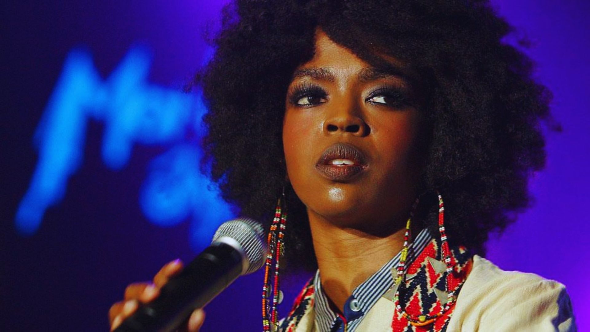 A woman with an afro hairstyle holds a microphone, ready to speak or perform.
