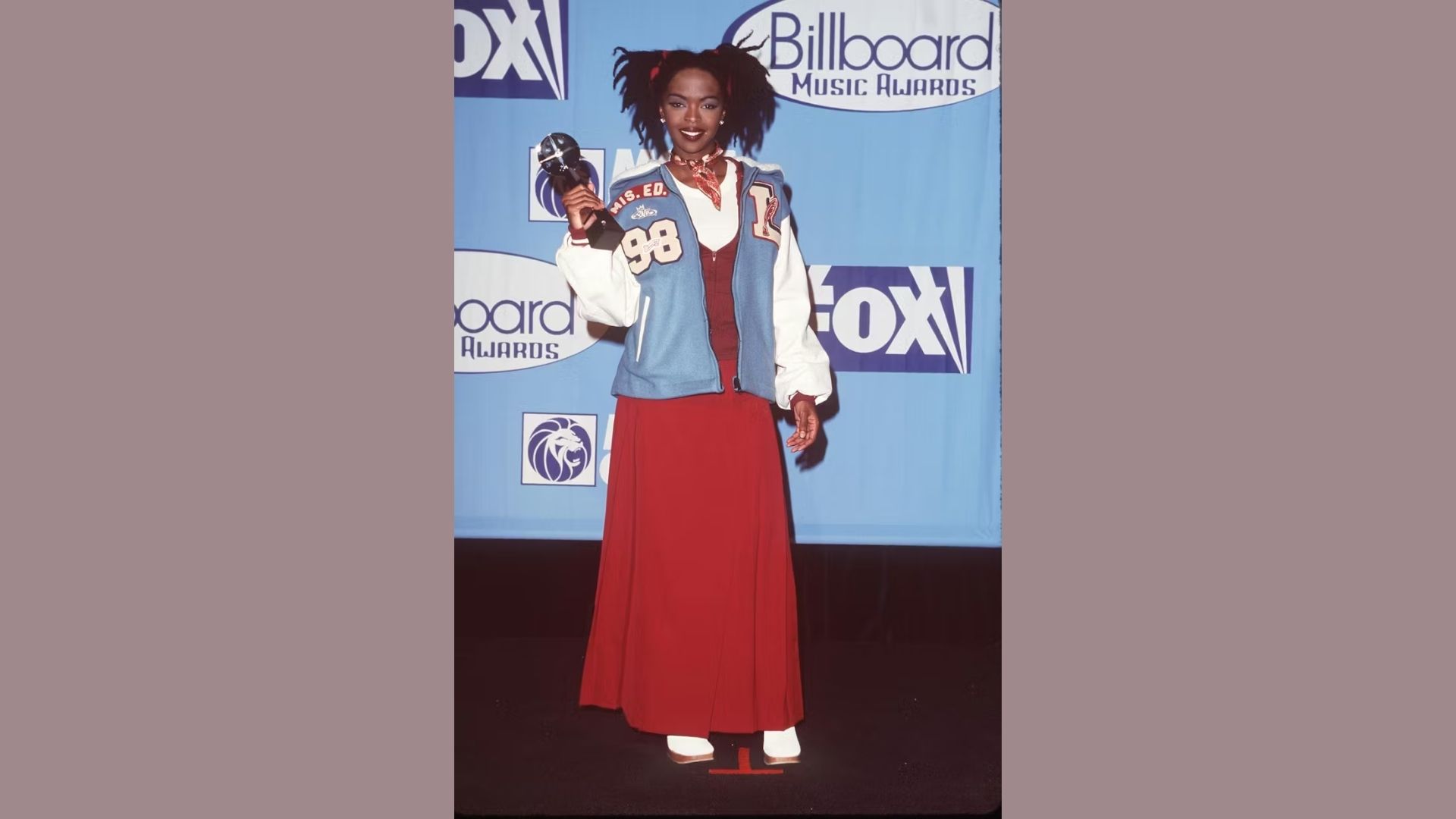 A woman wearing a red dress stands with an award in her hand, exuding joy and accomplishment.