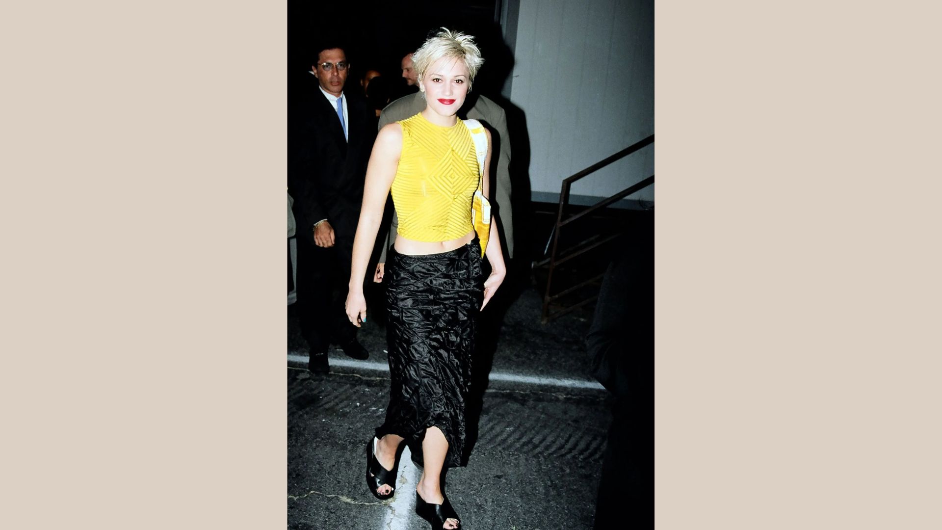 A woman wearing a yellow top and a black skirt stands confidently, showcasing her stylish outfit.