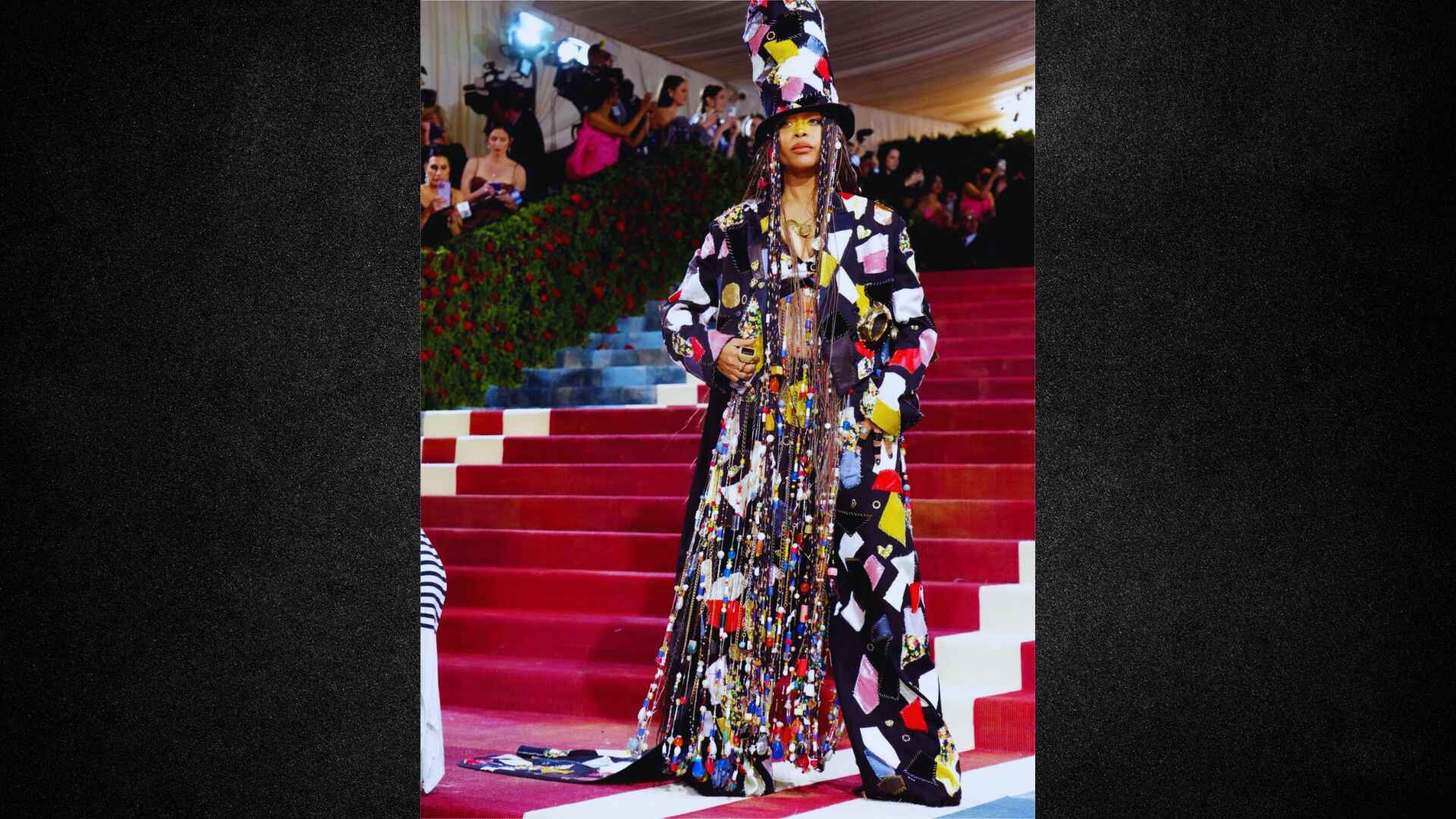 A woman in a colorful dress and hat poses on a set of stairs, showcasing her stylish outfit.