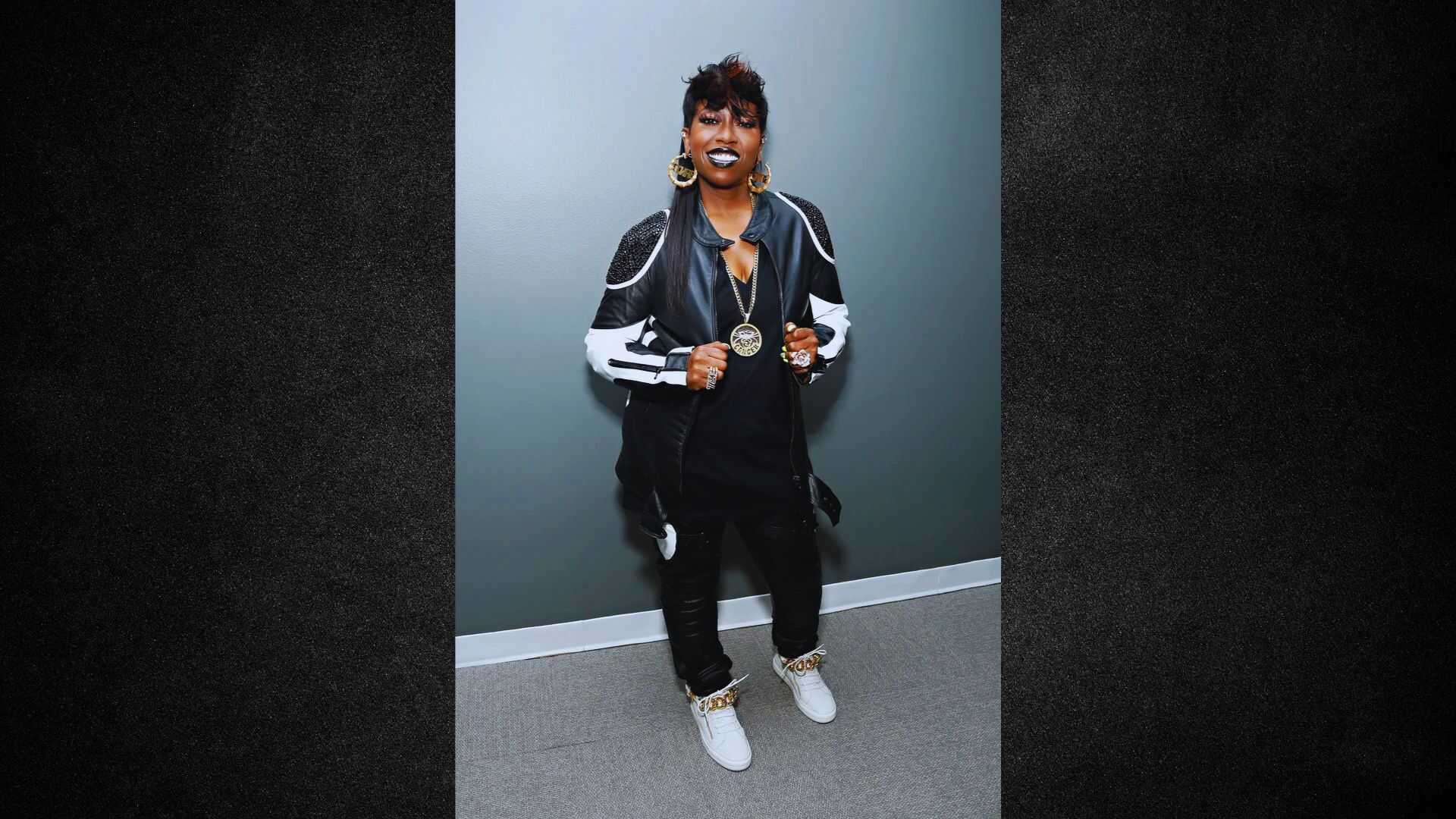 A woman in a black jacket and white sneakers stands confidently, showcasing a casual yet stylish outfit.
