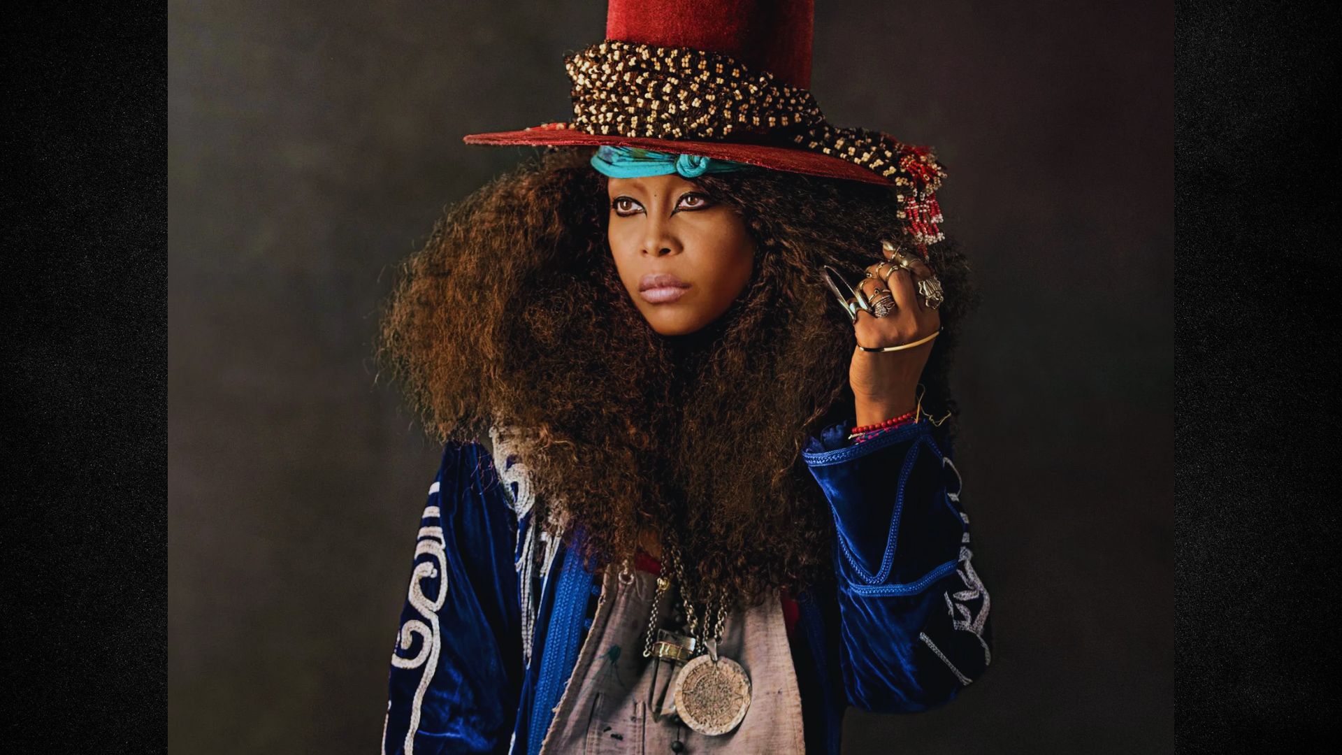 A woman with long hair wearing a large hat, standing outdoors in a bright, sunny setting.