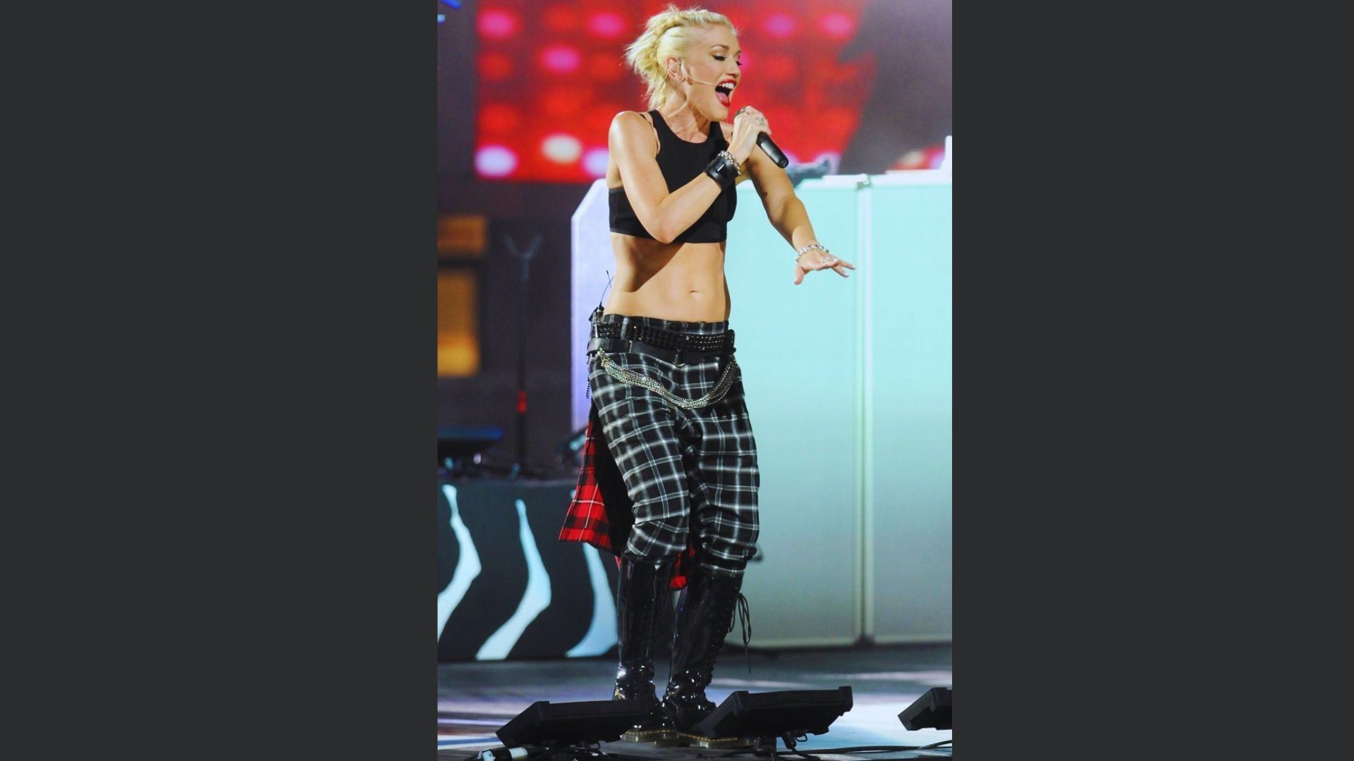 A woman in a crop top and plaid pants passionately sings into a microphone on stage.