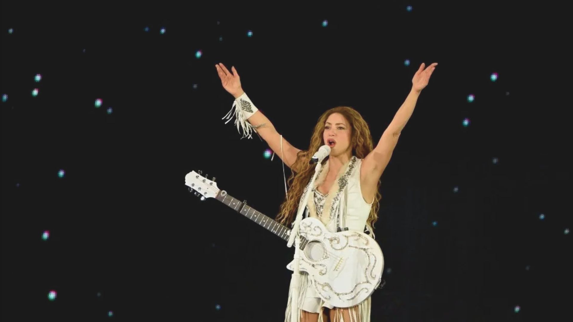 A woman in a white dress stands holding an electric guitar, ready to perform.