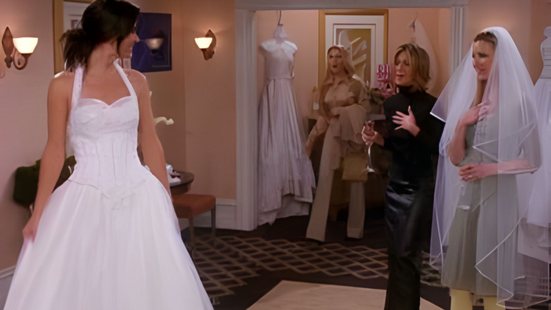 A woman in a wedding dress stands beside another woman, both smiling and celebrating a special moment together.