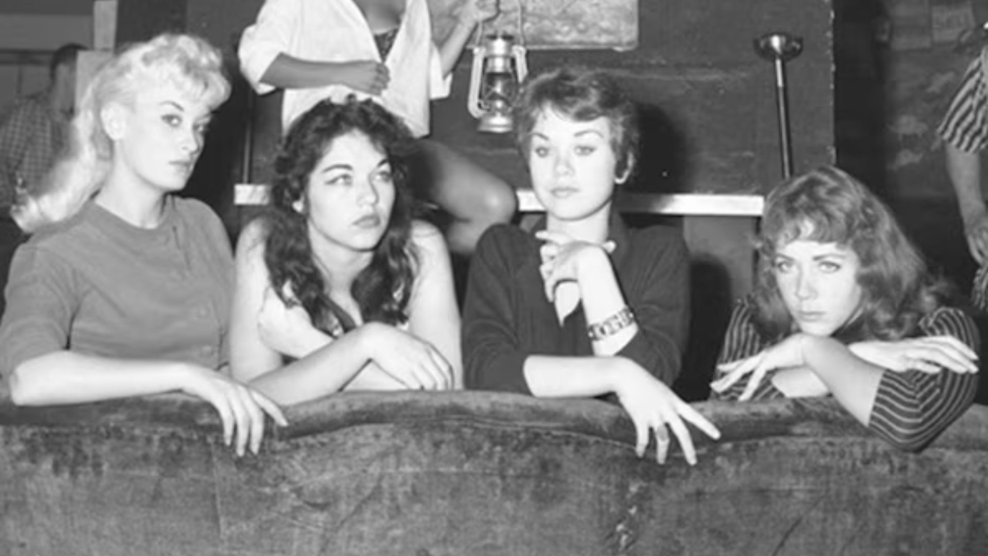 A group of women seated on a couch, engaging with a crowd in front of them.