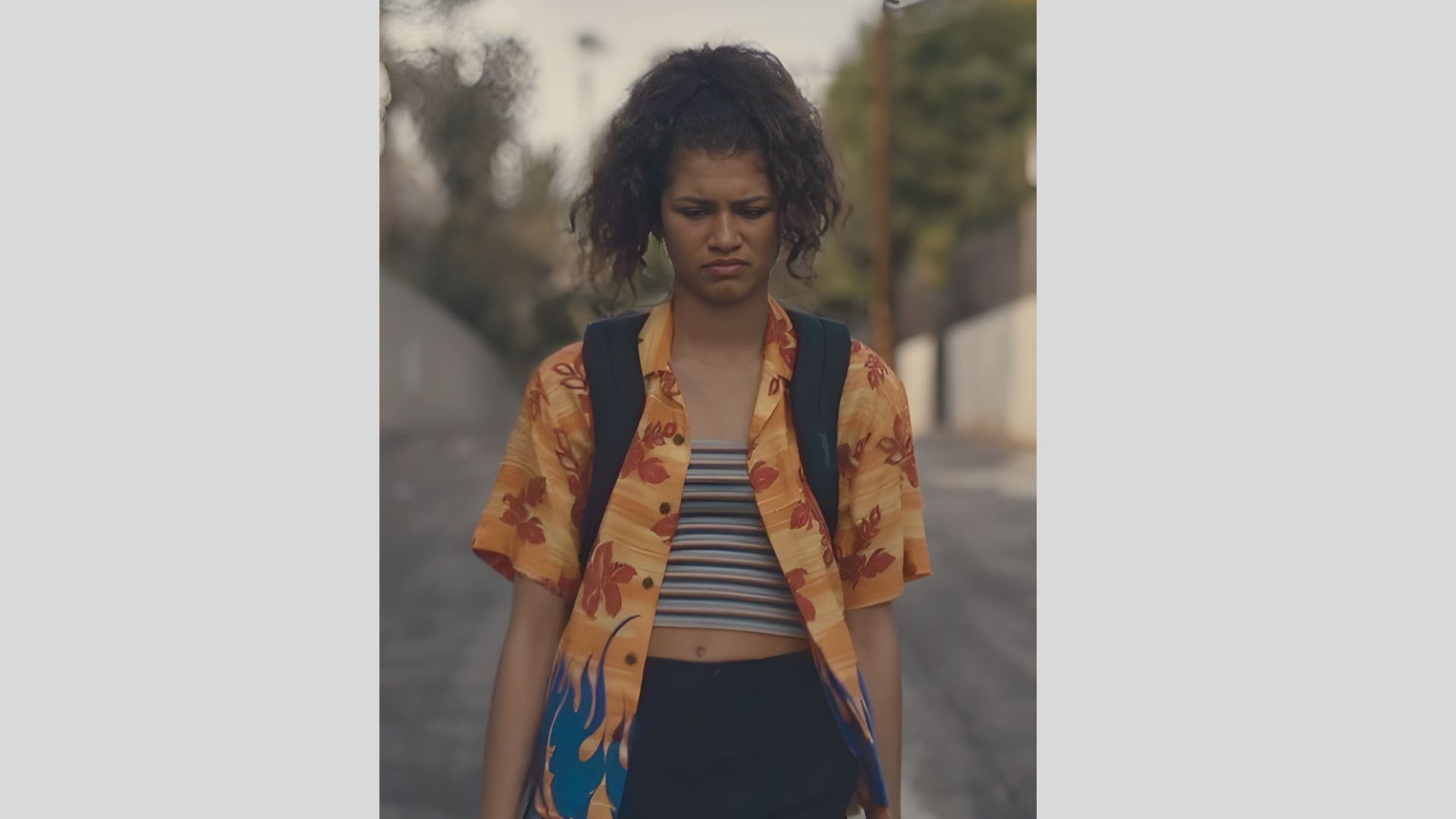 A woman in a floral shirt and black shorts stands, showcasing a vibrant and casual summer outfit.