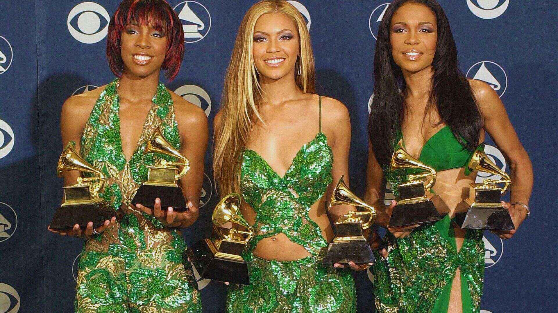 Three women in green dresses proudly display their Grammy Awards, celebrating their achievements in music.