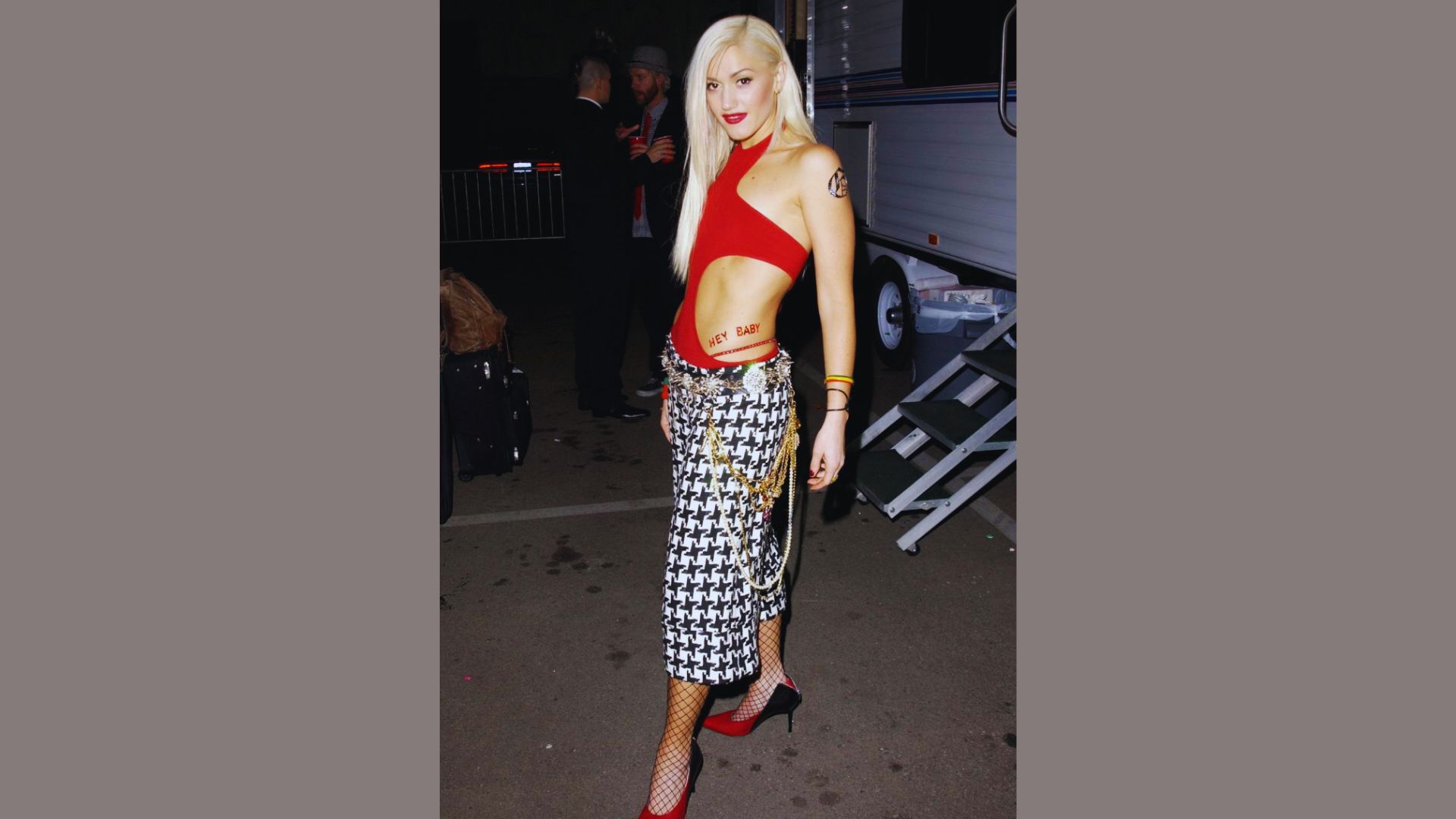 A woman wearing a red top and checkered pants stands confidently, showcasing her stylish outfit.