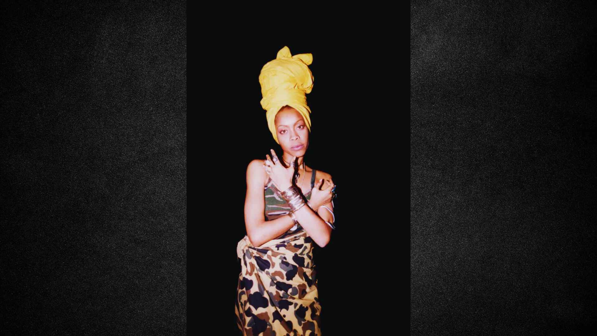 A woman in a yellow headscarf and a leopard print dress stands confidently, showcasing her unique style.