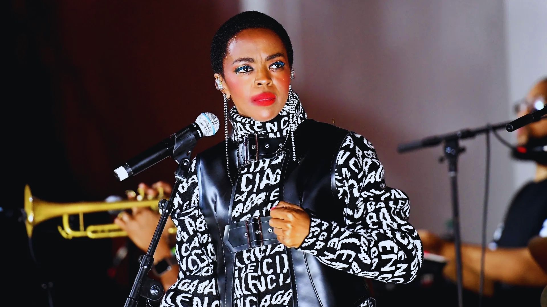 A woman wearing a black and white shirt and jacket passionately singing into a microphone on stage.