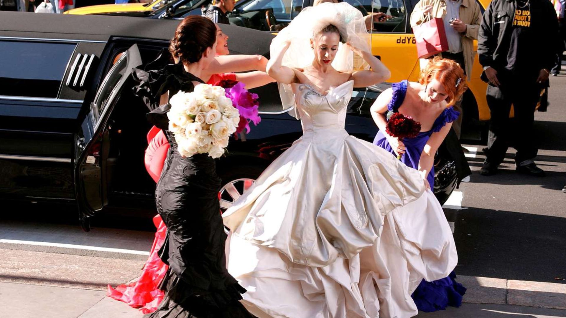 A woman in a wedding dress receives assistance from another woman, preparing for her special day.