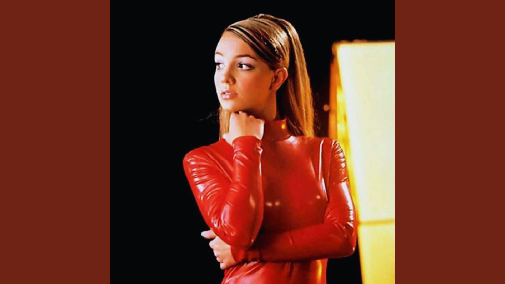 A woman poses confidently for the camera, wearing a striking red latex outfit that highlights her figure.