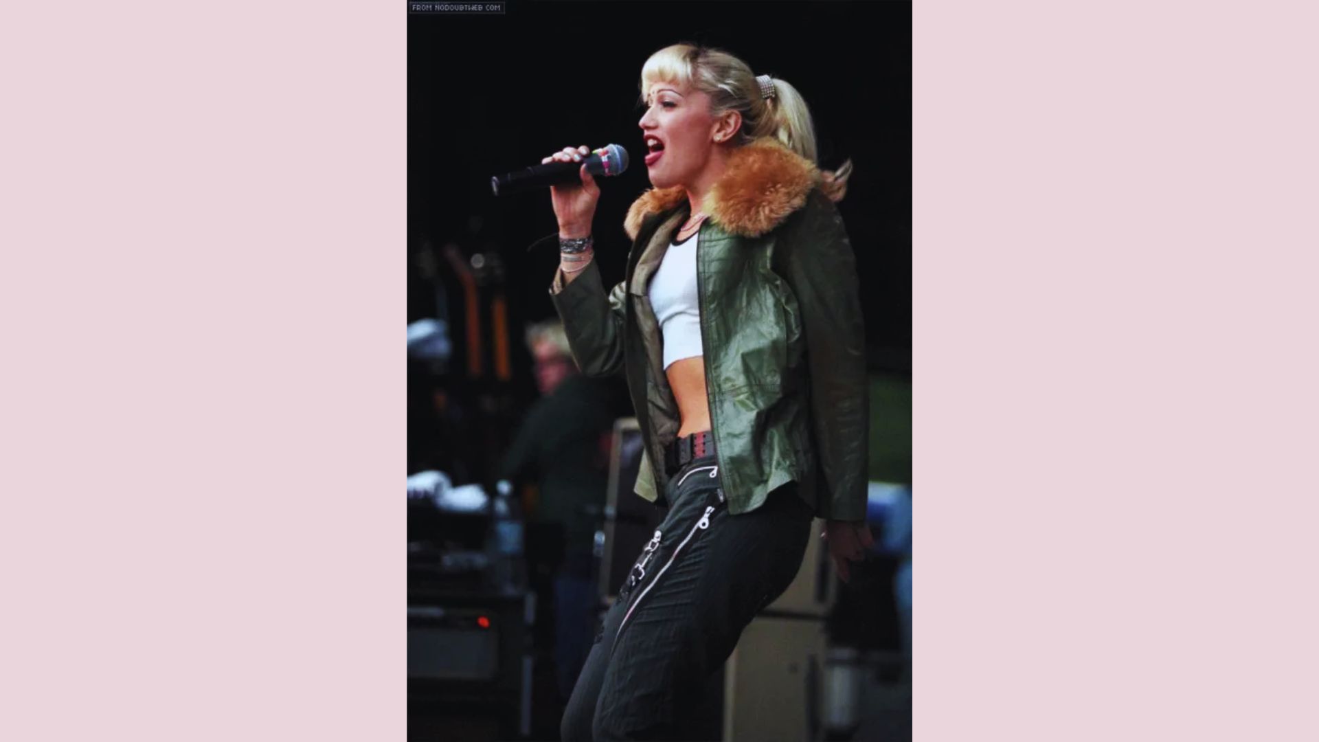 A woman wearing a green jacket singing into a microphone, engaging the audience with her performance.