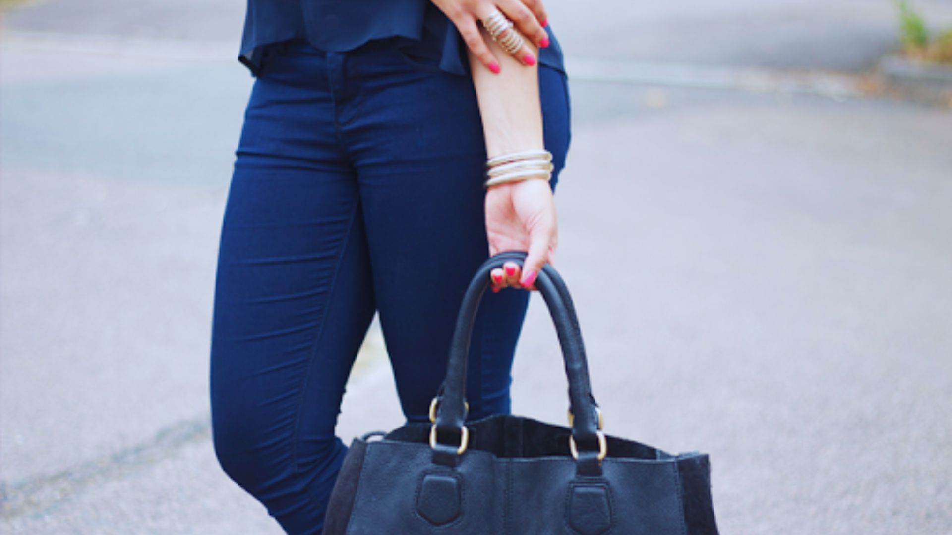 A woman wearing blue jeans and carrying a black handbag stands confidently.
