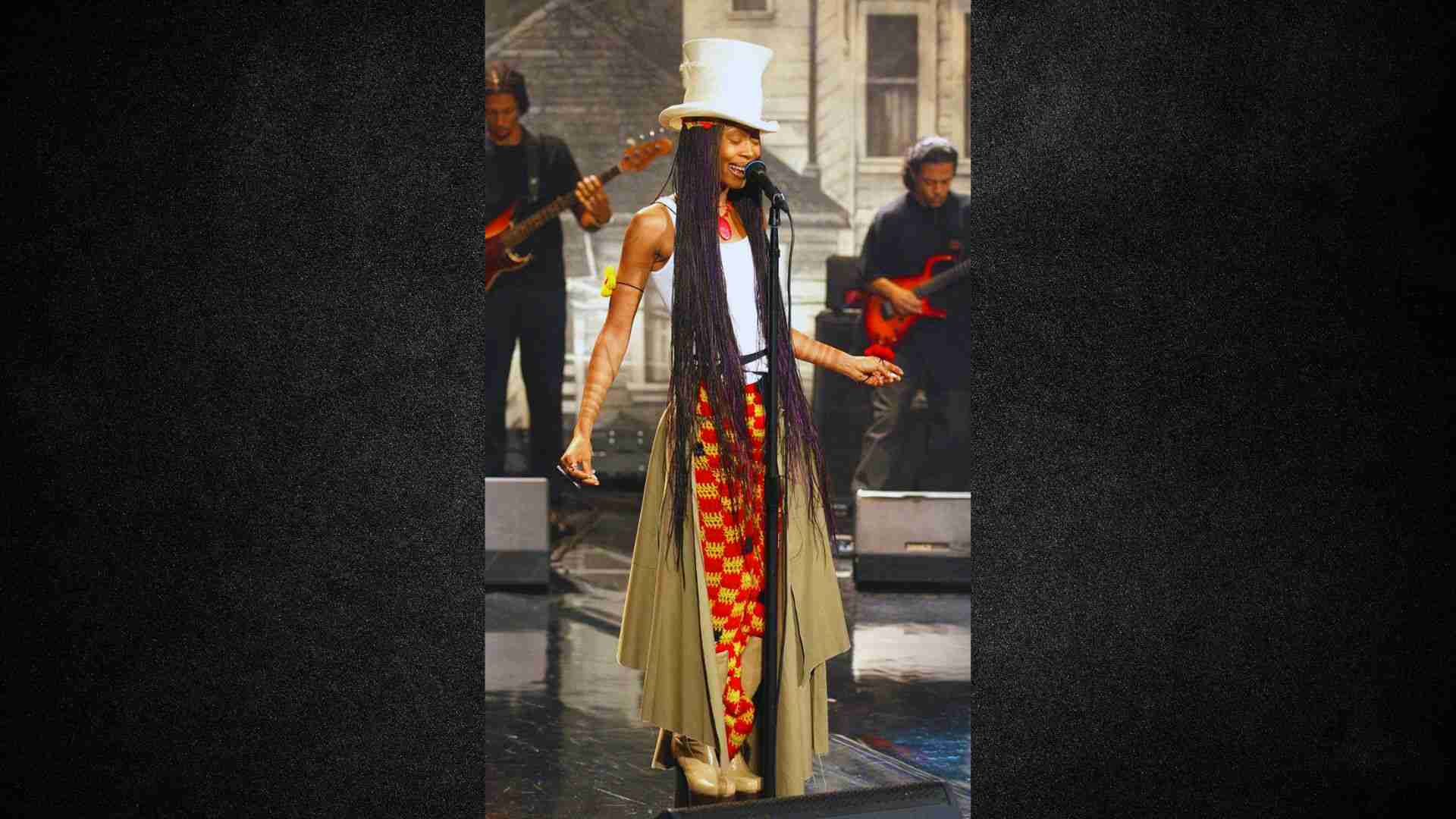 A woman with long hair wearing a hat performs on stage, engaging the audience with her presence.