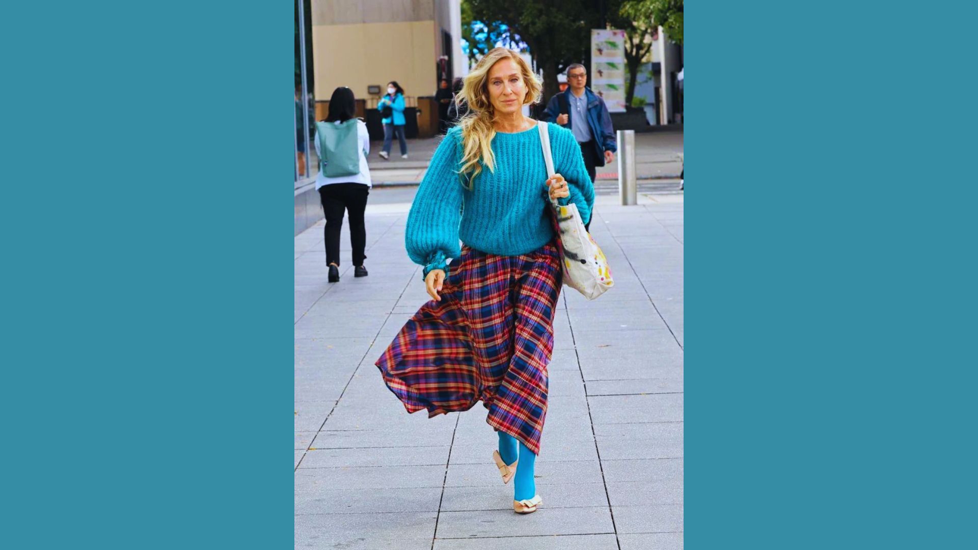 A woman in a blue sweater and plaid skirt walks down the street, showcasing a casual yet stylish outfit.
