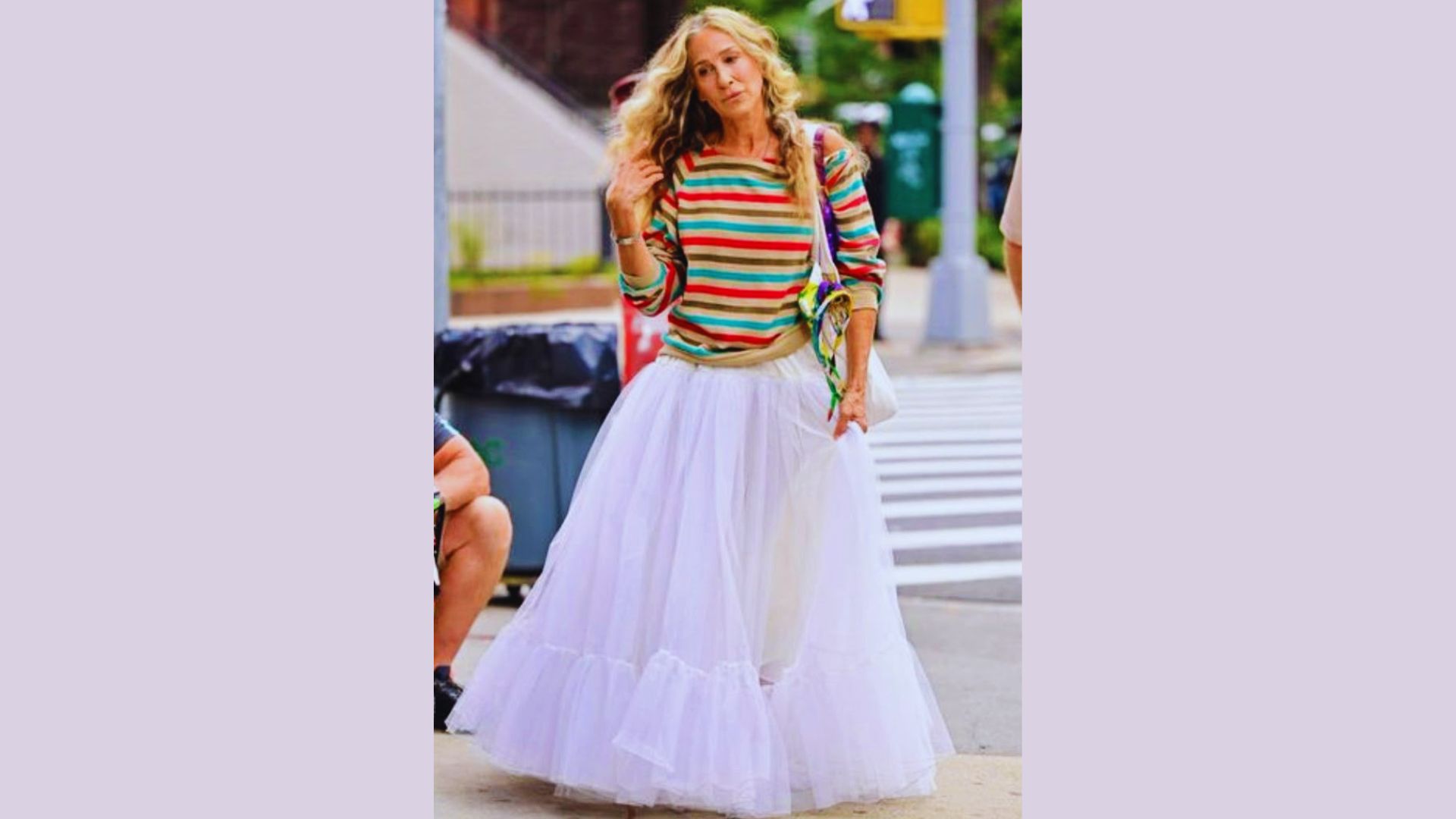 A woman in a vibrant shirt and skirt strolls down the street, showcasing her colorful outfit against the urban backdrop.