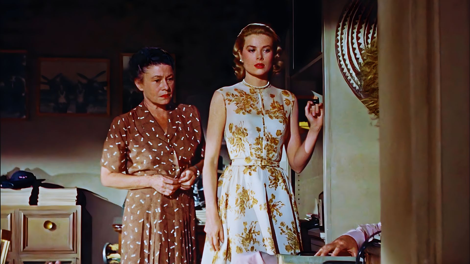 Two women in elegant dresses stand together in a well-decorated room, smiling and engaged in conversation.