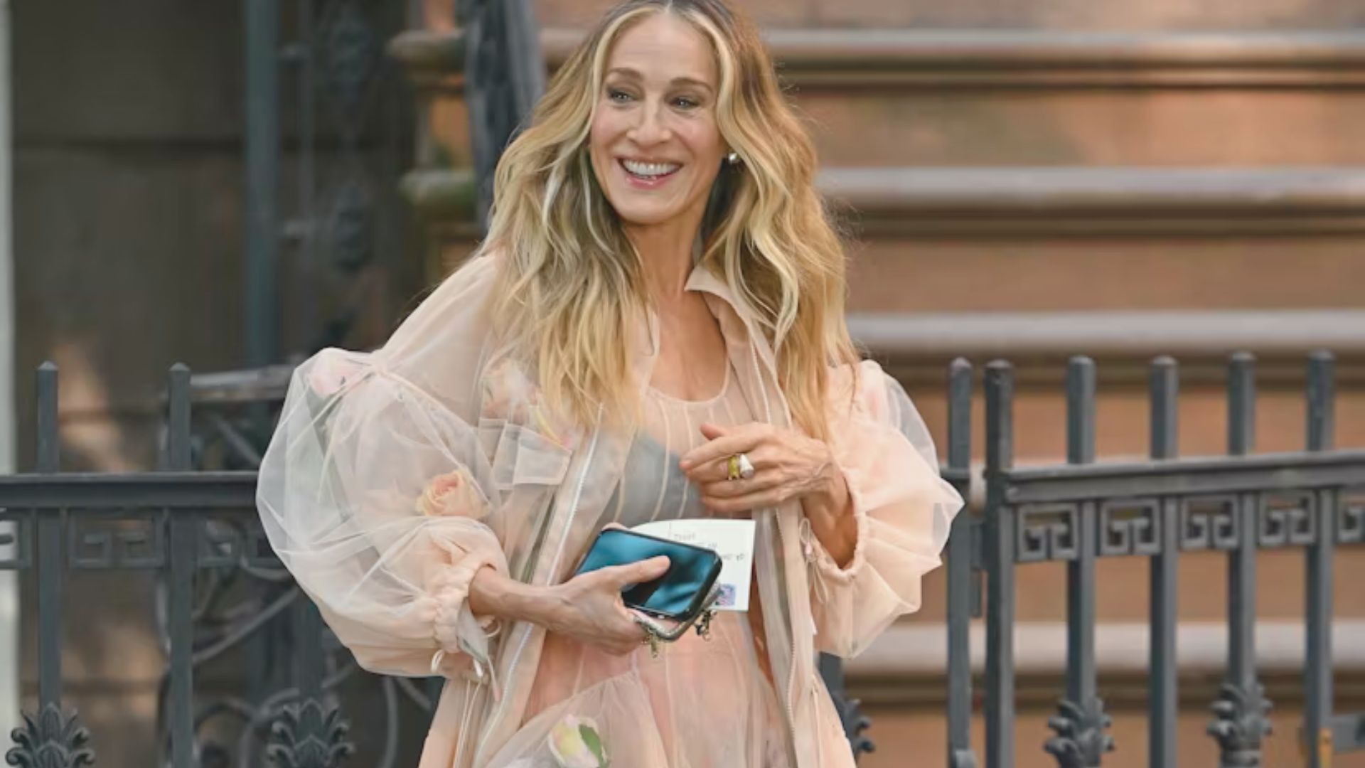 A woman in a pink dress, reminiscent of Carrie Bradshaw, walks confidently down a city street.