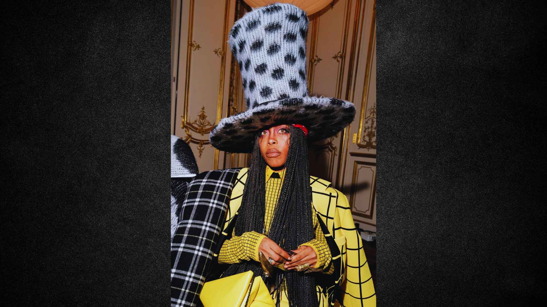A woman in a stylish hat and bright yellow outfit stands confidently, showcasing her vibrant fashion choice.