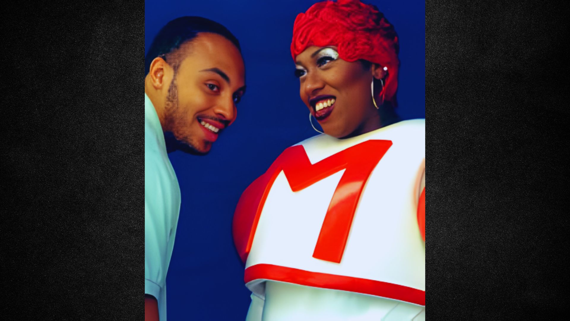 A man and woman in colorful costumes smile and pose together for a photo at a festive event.