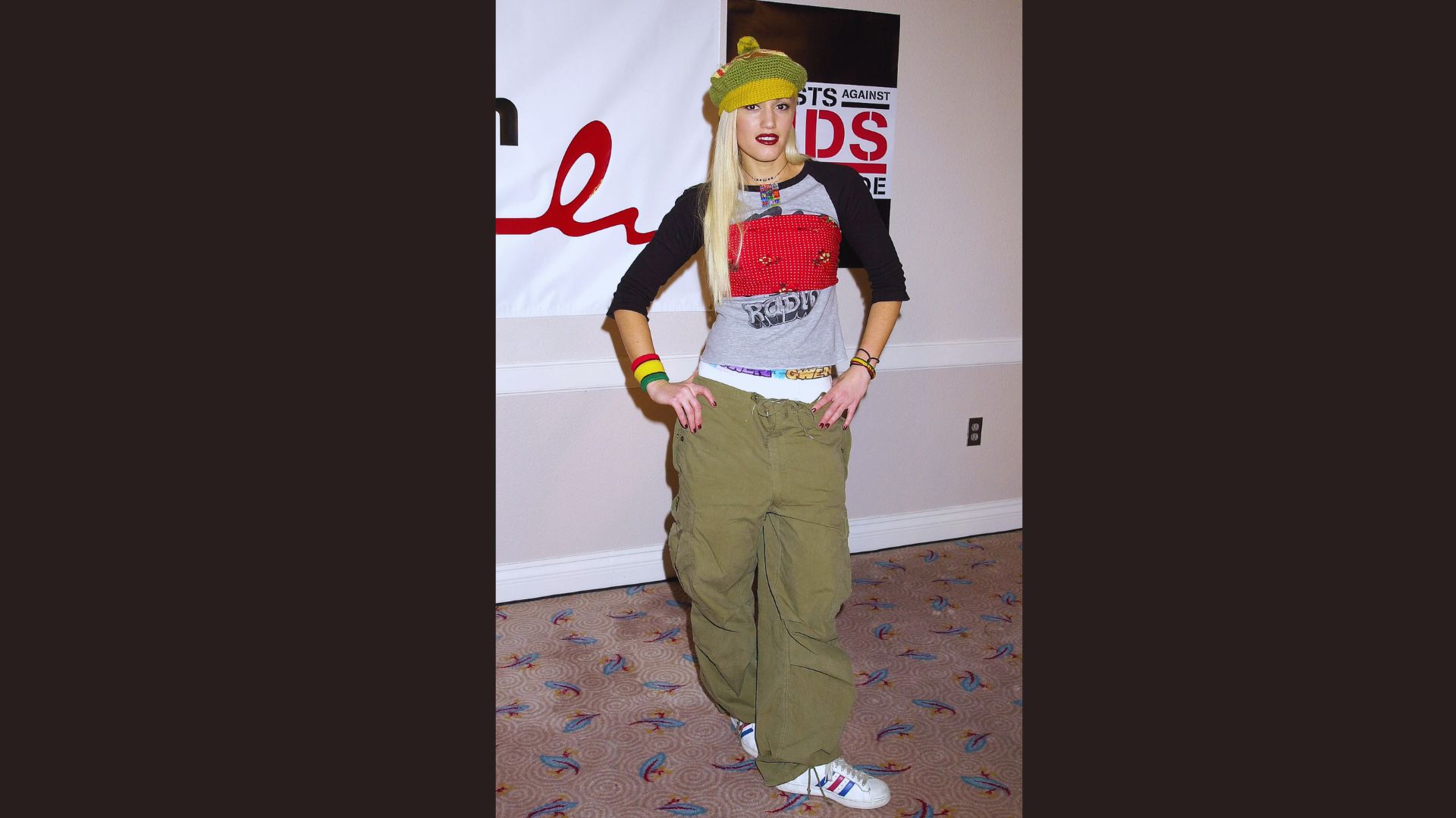 A woman wearing a stylish hat and green pants stands confidently, showcasing her unique fashion sense.