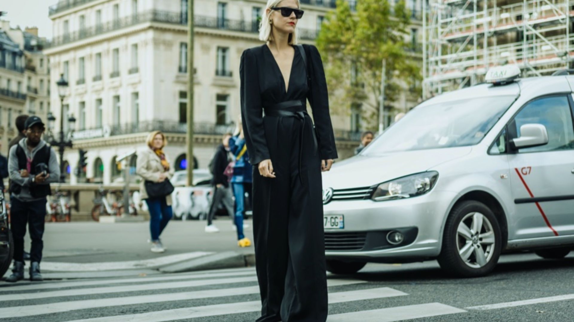 A woman in a black dress crossing the street, with city buildings in the background.