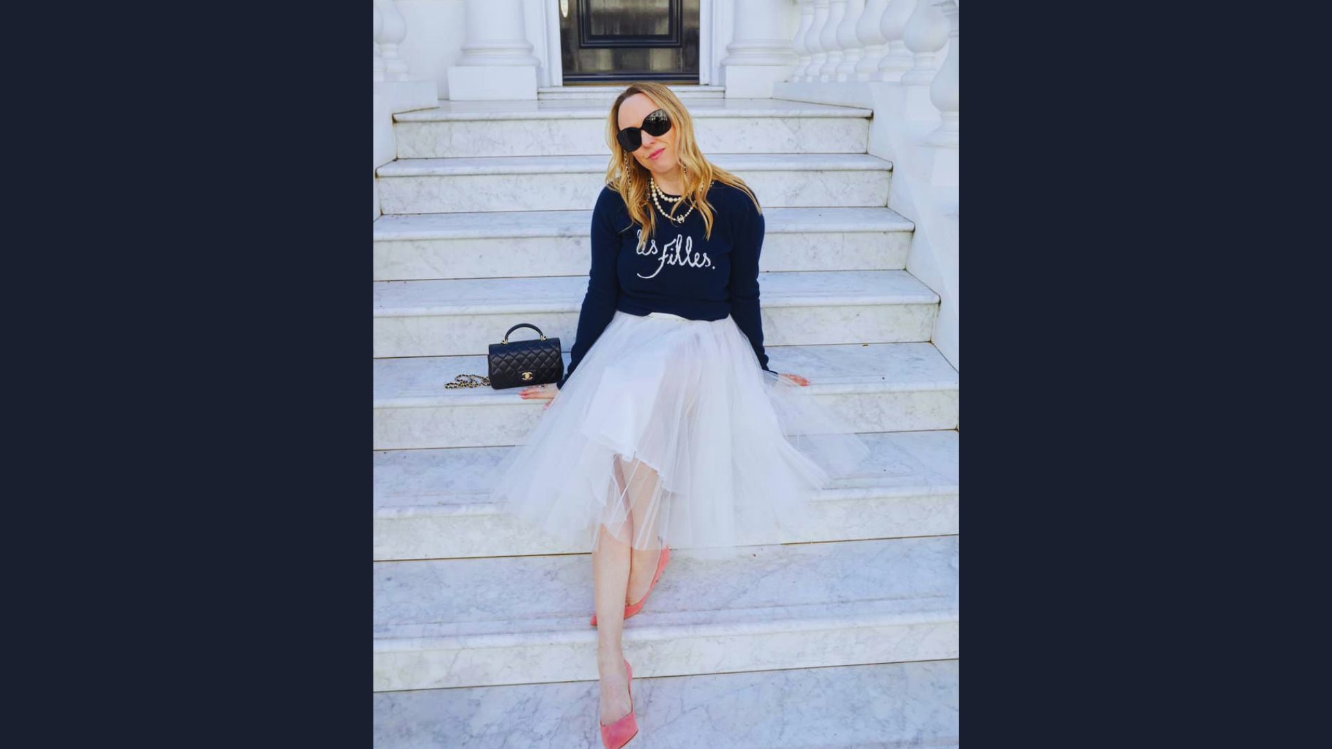A woman wearing a black sweater and a flowing white tulle skirt stands elegantly.
